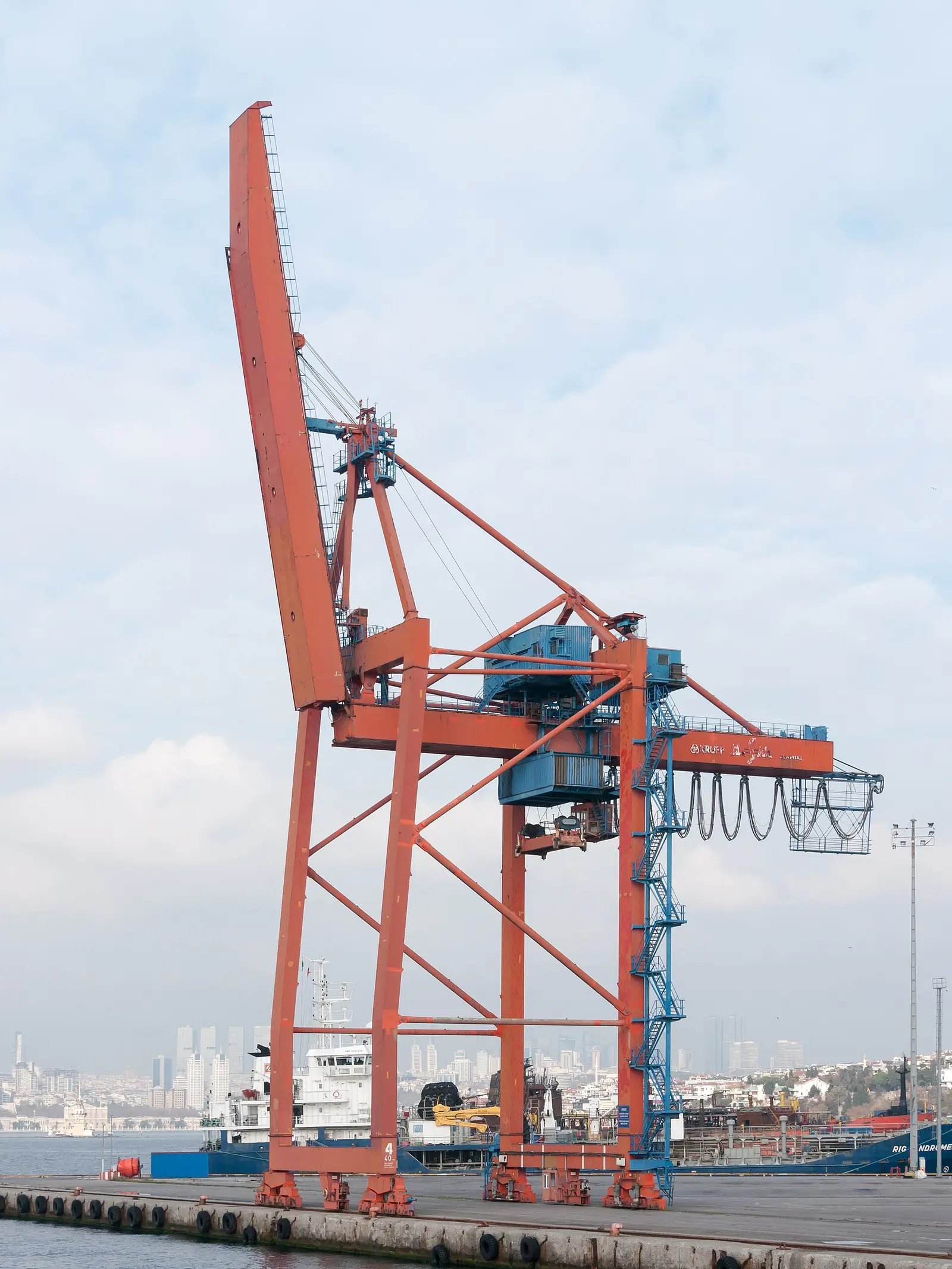 Haydarpaşa rıhtımında turuncu bir portal vinç; arkada İstanbul silueti ve bir yük gemisi